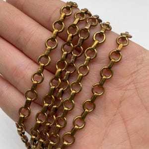May include: Close-up of several strands of antique brass-coloured chain. The chains are composed of small, interlocking circles and rectangular links. The chains are arranged in parallel lines, creating a textured surface. The chains are likely for jewellery or craft projects.