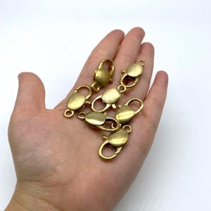 May include: A collection of gold-colored lobster claw clasps. The clasps are oval-shaped with a spring-loaded lever for secure closure. They are designed for jewelry making or crafting projects.
