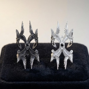 Puede incluir: Dos anillos ornamentados, uno negro y otro plateado, se exhiben sobre una superficie de terciopelo negro. Cada anillo presenta un dise&ntilde;o complejo y puntiagudo con una piedra oscura central. Los anillos tienen una est&eacute;tica art&iacute;stica &uacute;nica.