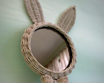 May include: A white wicker bunny mirror with a bow tie. The mirror is round and has a reflective surface.