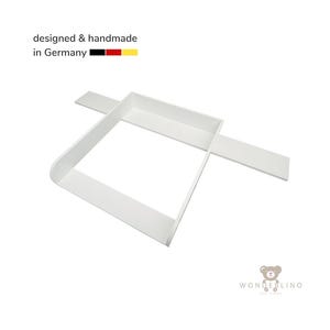 May include: A white wooden changing table topper with a rectangular frame and extended side panels. The text "designed & handmade in Germany" appears at the top with a German flag icon, and the "WONDERLINO" logo is visible at the bottom right.
