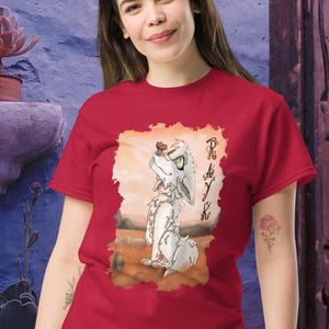 Può includere: T-shirt rossa con un'illustrazione di un lupo dei cartoni animati e la scritta "Rayk". Il lupo è bianco con occhi verdi, su uno sfondo di tramonto. La maglietta è di colore rosso unito.