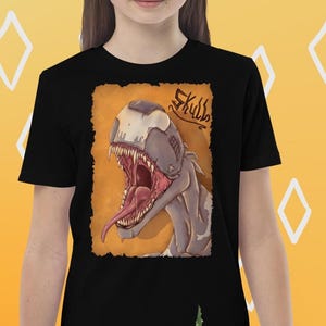 Könnte beinhalten: Schwarzes T-Shirt mit einer Illustration eines Dinosaurierschädels mit offenem Maul und langer Zunge. Das Wort "Skull" steht darüber. Der Hintergrund ist orange. Das T-Shirt wird von einer Person getragen.