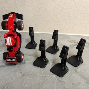 Peut inclure: Une voiture de course jouet rouge et noire avec le mot "Ferrari" imprimé à l'avant. La voiture a un design de casque blanc et rouge. Six supports noirs sont également dans l'image.