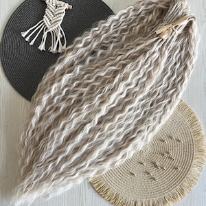 May include: A bundle of long, wavy, light beige synthetic hair extensions tied with a thin tan ribbon. The hair features a crimped texture throughout the length, creating a voluminous appearance. The extensions are arranged in a fan shape.