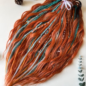 Puede incluir: Un conjunto de rastas naranjas, turquesas y blancas atadas con una cinta blanca. Las rastas tienen una textura ondulada y están decoradas con costuras blancas. Dos piñas se encuentran en el fondo.