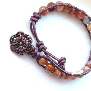 May include: A brown leather bracelet with a copper flower charm and multi-colored agate beads.