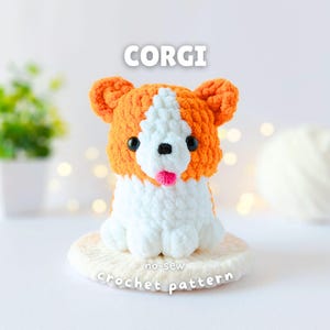 Può includere: Una figura di cane Corgi all'uncinetto in peluche con filato arancione e bianco, occhi in plastica nera, naso nero e una piccola lingua rosa. Il testo CORGI e no-sew crochet pattern è visibile attorno alla figura su una base bianca.