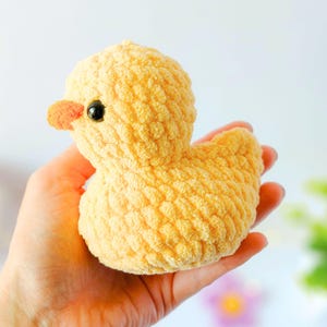 May include: A handmade, yellow crochet duck with a textured surface. The duck has a small orange beak and a black eye. The plush toy is a soft, cuddly item.