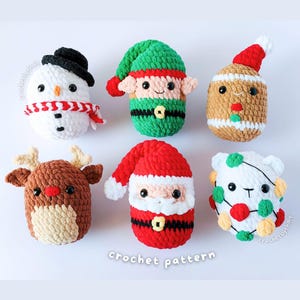 Puede incluir: Seis pequeñas figuras de peluche tejidas a ganchillo, dispuestas en dos filas. La fila superior incluye un muñeco de nieve con sombrero negro, un elfo en verde y rojo, y una figura de pan de jengibre. La fila inferior muestra un reno, Papá Noel y un oso blanco con luces.