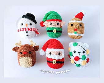 May include: Six small, round, crocheted plush figures arranged in two rows. The top row features a snowman with a black hat, an elf in green and red, and a gingerbread person. The bottom row shows a reindeer, Santa Claus, and a white bear with lights.
