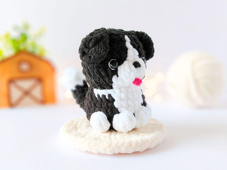 May include: A small, handmade crochet dog plushie featuring black and white yarn. The figure has a white face, chest, and paws, with black ears and body. It has two black plastic eyes and a small, bright pink yarn tongue protruding from its mouth.