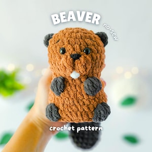 以下が含まれることがあります： 手作りの茶色と灰色の編み物ビーバーのおもちゃ。ビーバーは黒い目、白い歯、黒い尾を持っています。画像には「BEAVER」と「crochet pattern」という文字が表示されています。