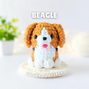 May include: A plush beagle toy made of brown and white yarn with black eyes and a pink nose. The text BEAGLE is displayed above the toy, and the text no-sew crochet pattern is printed on the circular white base beneath the plush figure.