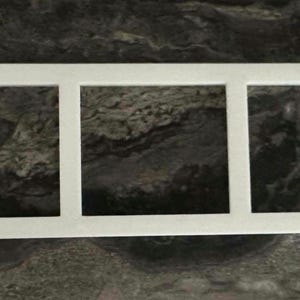 May include: A white rectangular frame with three sections. The frame has a straightforward design with three equal openings. The background is a dark, mottled surface, contrasting with the bright white frame.