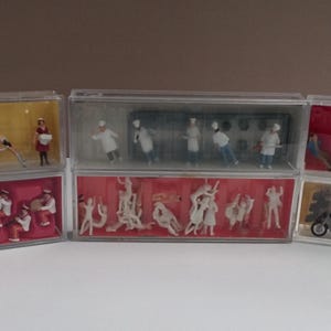 May include: Miniature figurines displayed in clear plastic cases. The figurines represent different scenes, such as musicians, chefs, and motorcyclists. The cases feature coloured backgrounds of red, yellow, and beige.