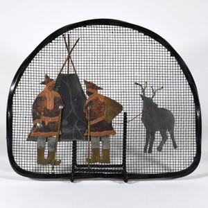 May include: A decorative metal art piece featuring two figures with walking sticks, a teepee, and a deer. The figures and deer are silhouetted against a mesh background within a black frame. The figures have copper and bronze tones.