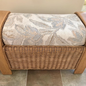 May include: A rectangular storage bench featuring a light-coloured wooden frame with curved ends. The top cushion is upholstered in a cream fabric with a grey and tan floral pattern. The front panel is constructed from woven natural wicker material.