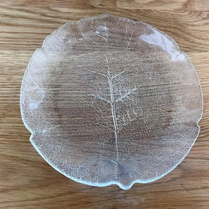 May include: A clear glass plate shaped like a large leaf with a textured surface that mimics natural veins. The plate features a crackled glass effect throughout its circular form, with an irregular, organic edge that follows the leaf outline.