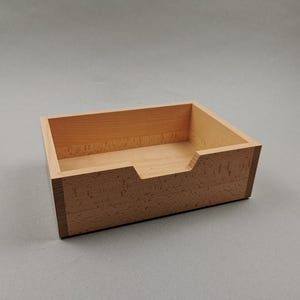 Op de afbeelding: Een kleine, rechthoekige houten doos met één compartiment. De doos is gemaakt van licht hout met een natuurlijke afwerking.