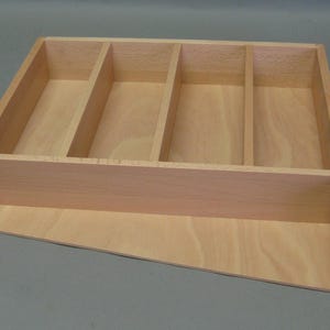 Könnte beinhalten: Ein Bestecktablett aus Holz mit vier Fächern. Das Tablett ist aus hellem Holz und hat eine natürliche Oberfläche.