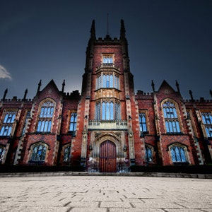 May include: A large, red brick building with a tall tower and many windows. The building has a dark, stormy sky in the background.