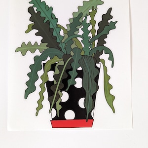 Puede incluir: Una pegatina con una ilustración estilizada de una planta de interior. La planta tiene hojas verdes largas y onduladas y está en una maceta negra con lunares blancos y una base roja. Fondo blanco.