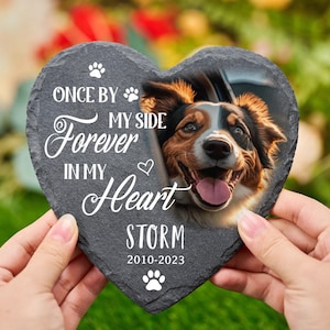 Könnte beinhalten: Herzförmige Schiefertafel-Gedenktafel mit einem Hundefoto. Der dunkelgraue Schiefer hat weißen Text: "Once by my side, forever in my heart, Storm 2010-2023." Pfotenabdrücke und ein Herz sind ebenfalls enthalten.