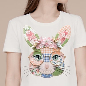 May include: White t-shirt featuring a colorful patchwork bunny face with glasses, eyelashes, and whiskers. The bunny has floral and gingham patterns, with a pink nose and a flower crown. The design is centered on the shirt.