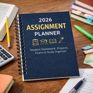 Op de afbeelding: Een marineblauwe 2026 Assignment Planner met spiraalbinding. De cover heeft gouden tekst en iconen, waaronder de woorden "Student Homework, Projects, Exams & Study Organiser". Een potlood, rekenmachine en boeken staan op de achtergrond.