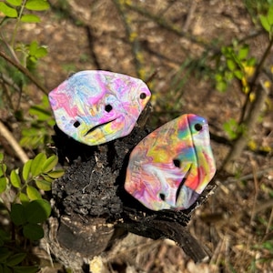 Könnte beinhalten: Zwei bunte, abstrakte, wirbelförmige, dekorative, geometrische Formen aus Kunststoff mit Löchern. Die Formen sind rosa, gelb, blau, grün und orange.