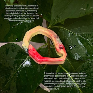 May include: A recycled plastic bracelet with a distinctive marbled pattern. The bracelet has a curved form, with red and yellow hues, set against a background of green leaves. The image text discusses recycling and sustainability.