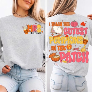 Könnte beinhalten: Ein hellgraues Sweatshirt mit einer farbenfrohen Herbstgrafik. Auf der Vorderseite steht der Text "MRS William" mit einem Kaffeebecher- und Sahne-Design. Auf der Rückseite steht "I teach the cutest pumpkins in the patch" mit Kürbissen, Blättern und Schulmaterial.