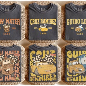 May include: Six charcoal gray t-shirts featuring designs from the Cars movie. Each shirt displays a character's name in a vintage font, along with the text "EST. 2006 CARS" and a cartoon image of the character. The designs include Tow Mater, Cruz Ramirez, and Guido Luigi.