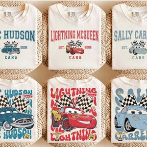 May include: White t-shirts featuring designs from the movie "Cars." Each shirt displays a character's name, a car illustration, and the year 2006. The designs include Doc Hudson, Lightning McQueen, and Sally Carrera, with checkered flags.