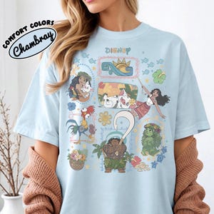May include: Light blue t-shirt featuring Disney characters from the movie Moana. The shirt has a crew neck and short sleeves. The text "Disney" is printed at the top. The shirt is made of a soft, comfortable material.