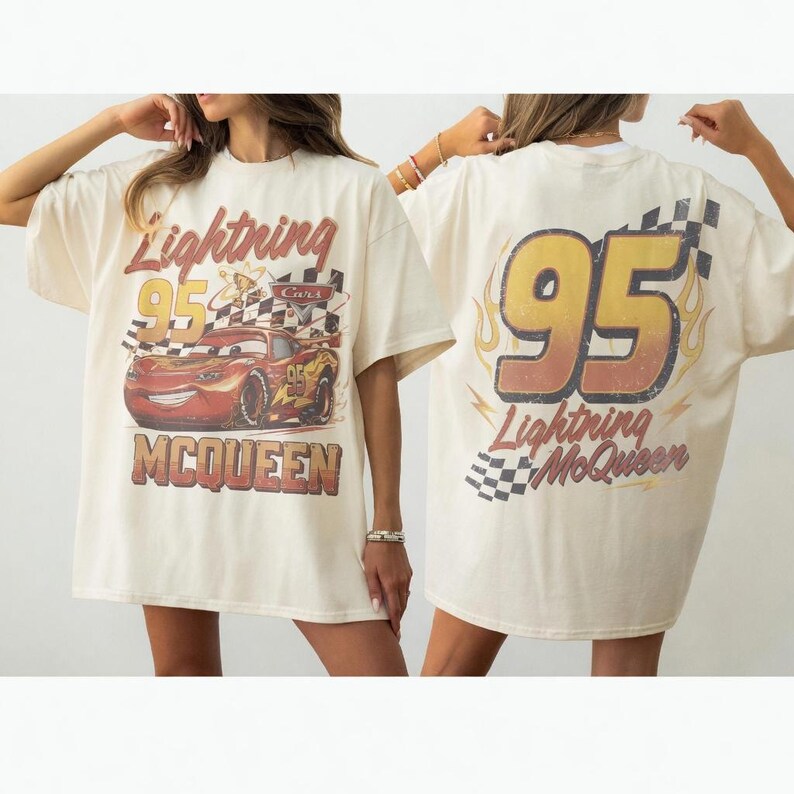 Op de afbeelding: Een off-white t-shirt met een afbeelding van de rode raceauto Lightning McQueen met de tekst Lightning McQueen en 95 op de voorkant. De achterkant toont een grote 95 met vlamaccenten, geblokte patronen en de tekst Lightning McQueen.