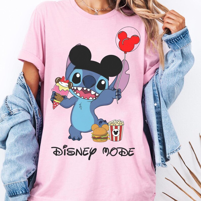 Puede incluir: Camiseta rosa claro con un personaje de dibujos animados con orejas negras, sosteniendo un globo rojo, helado y una hamburguesa. Las palabras "DISNEY MODE" est&aacute;n impresas en negro debajo.