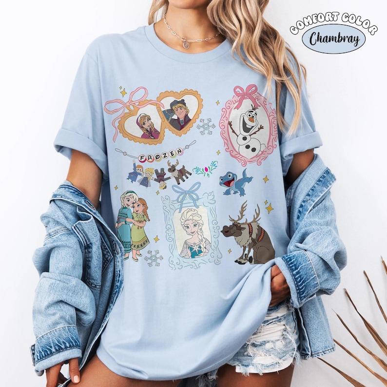 Peut inclure: Un t-shirt bleu clair avec une impression graphique des personnages du film Frozen, incluant Anna, Elsa, Olaf, Sven et Kristoff. Le motif comprend des cadres en forme de c&oelig;ur, une banni&egrave;re avec le texte Frozen et des flocons de neige.