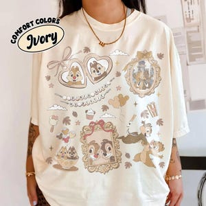 Könnte beinhalten: Elfenbeinfarbenes T-Shirt mit einem Grafikdesign mit Zeichentrickfiguren in herzförmigen Rahmen und einem Schloss. Das Shirt enthält den Text "Doney with my bestie" und "Comfort Colors Ivory".