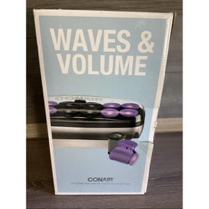May include: A Conair Waves & Volume hair setter box featuring a light blue background with white text. The box displays a black and silver heating unit with purple rollers and a separate purple hair clip, labeled as 12 flocked rollers.