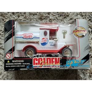 May include: A die-cast metal Pepsi-Cola coin bank in a classic truck design. The truck is white with red accents and gold wheels, featuring Pepsi-Cola branding. The packaging includes the text "Golden Classic Gift Bank."