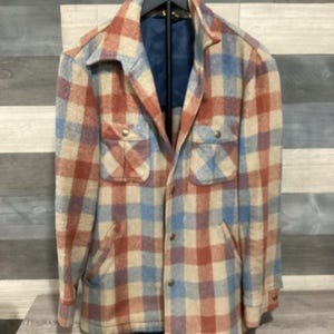 Puede incluir: Chaqueta vintage a cuadros en rojo, azul y beige. La chaqueta tiene dos bolsillos en el pecho y dos bolsillos inferiores, con botones. El forro interior es azul marino liso.