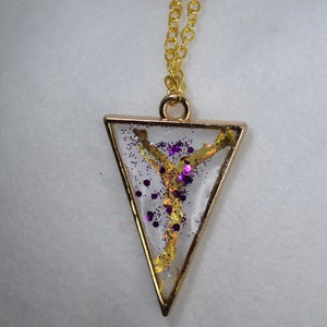 Puede incluir: Collar con colgante de triángulo dorado, relleno de resina transparente con purpurina dorada y morada.
