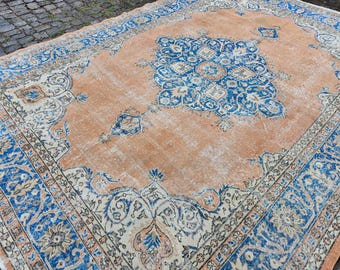 May include: An antique, rectangular rug with a central medallion design. The rug features a peach-colored field with a large, ornate blue and white central pattern. A blue and white border frames the rug, adding to its vintage aesthetic.