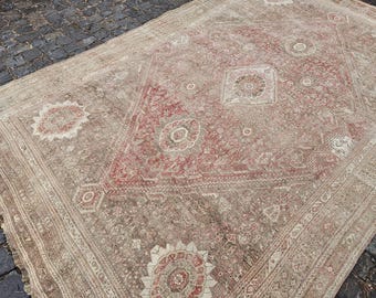 May include: A large, rectangular rug with a central diamond pattern in shades of red and beige. The rug features intricate floral and geometric designs, with a border of repeating patterns. The overall color palette is muted, giving it a vintage appearance.