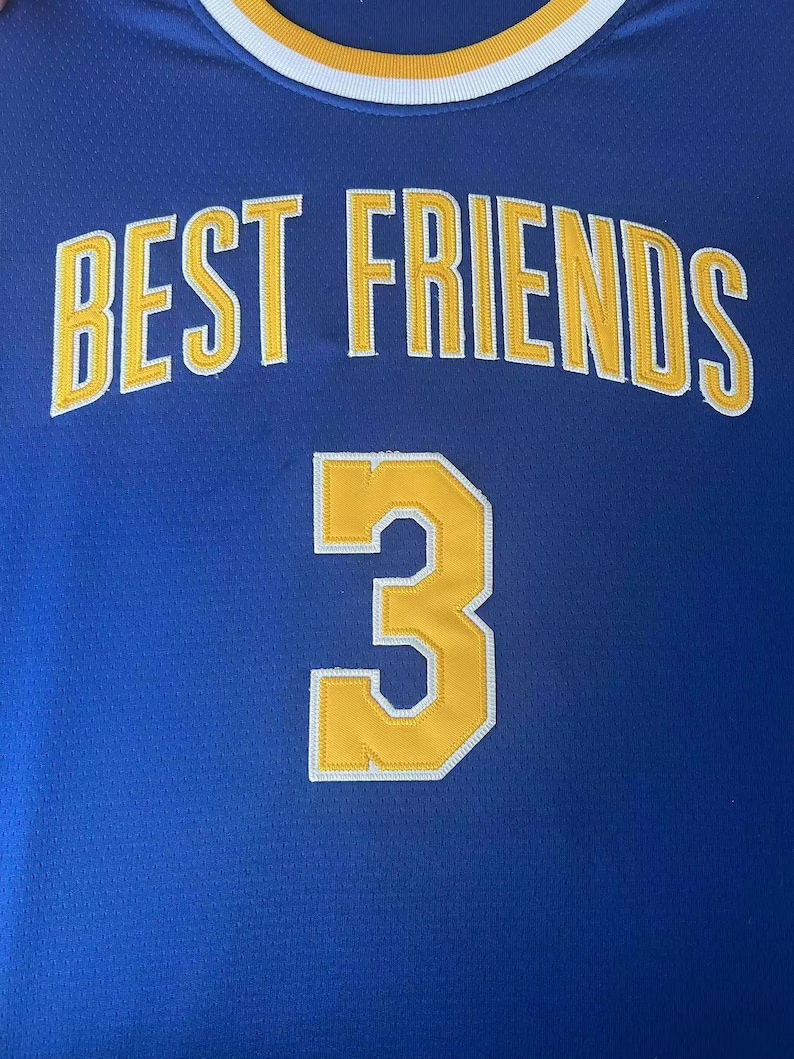 May include: A blue athletic jersey featuring the text BEST FRIENDS in yellow block letters with white outlines, and the number 3 in yellow with a white outline below. The neckline has a white and yellow striped ribbed trim design.