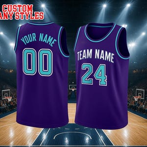 May include: Two purple basketball jerseys with teal and white trim. The left jersey features the text YOUR NAME and the number 00 in teal with white outlines. The right jersey displays TEAM NAME and the number 24 in white with teal outlines.