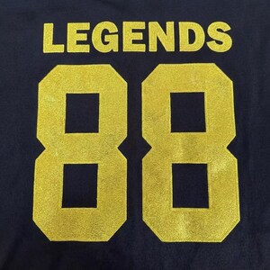 May include: A dark navy blue fabric background featuring the word LEGENDS printed in a bold, gold-colored font above the large number 88, which is also rendered in a matching gold-colored, textured, block-style typeface.
