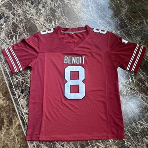 Puede incluir: Una camiseta de f&uacute;tbol granate con el nombre "BENOIT" y el n&uacute;mero "8" en letras blancas. La camiseta tiene cuello en V y rayas blancas en las mangas. La camiseta est&aacute; hecha de un material atl&eacute;tico transpirable.